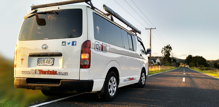 Trustee Traveller Camper von Chilli Rentals auf einer Landstraße in Neuseeland, Heckansicht